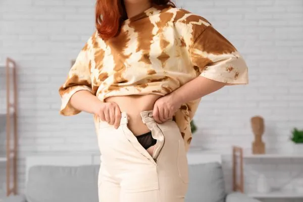 Image of woman trying to do her trousers up after pregnancy weight gain Hertfordshire